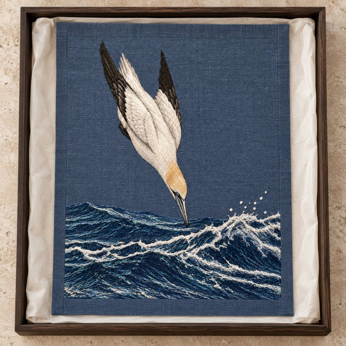 Gannet in the Whitewater Plunge visual mockup shown as a textile panel in a collection tray, with the design on slate-blue linen.
