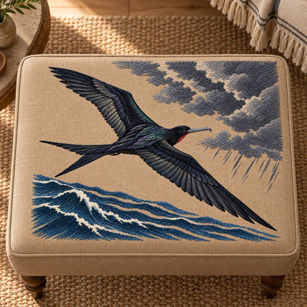 Frigatebird embroidery design in a digital mockup of A mushroom-linen large rectangular upholstered footstool top photographed from nearly overhead, top of motif toward top of photograph, cloud above and ocean below. Placement inspiration for Study 06.