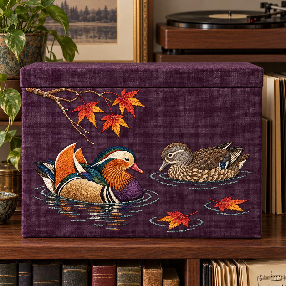 Mandarin Duck Pair embroidery design in a digital mockup of A landscape embroidered front on a linen-covered music-score storage box, box standing upright on a shelf in a quiet listening room, lid uninterrupted and ratio preserved. Placement inspiration for Study 19.