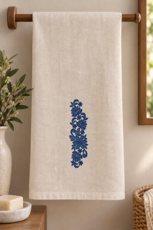 Styled linen guest towel mockup with a single deep smoky indigo blue fan flower botanical spray embroidered on pale linen; the complete motif has clear fabric around it.