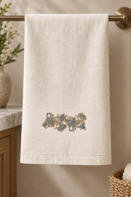 Ivory linen guest towel with a small petrol blue and champagne acanthus scroll above the hem.