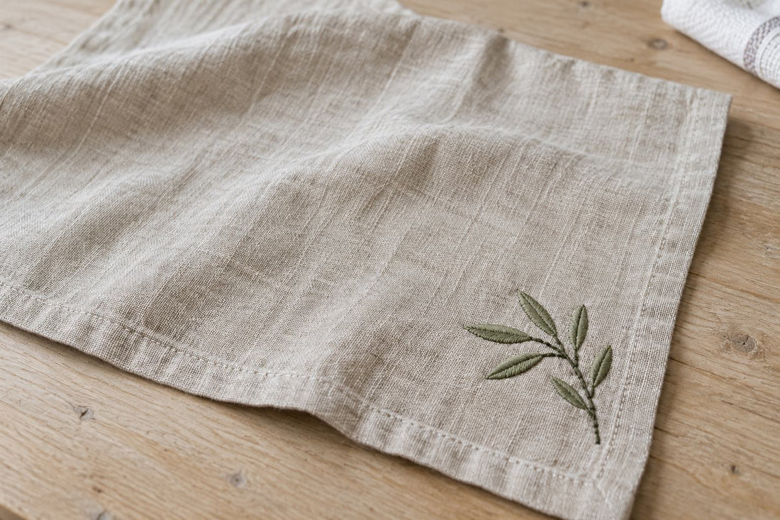 Dry oatmeal linen napkin with a green embroidered sprig on a wooden textile worktable