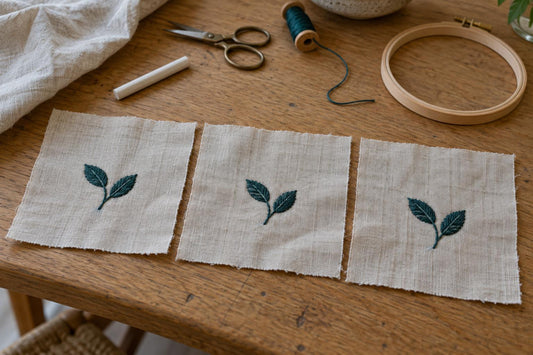 Three linen practice squares with matching teal leaf embroidery on a sewing worktable