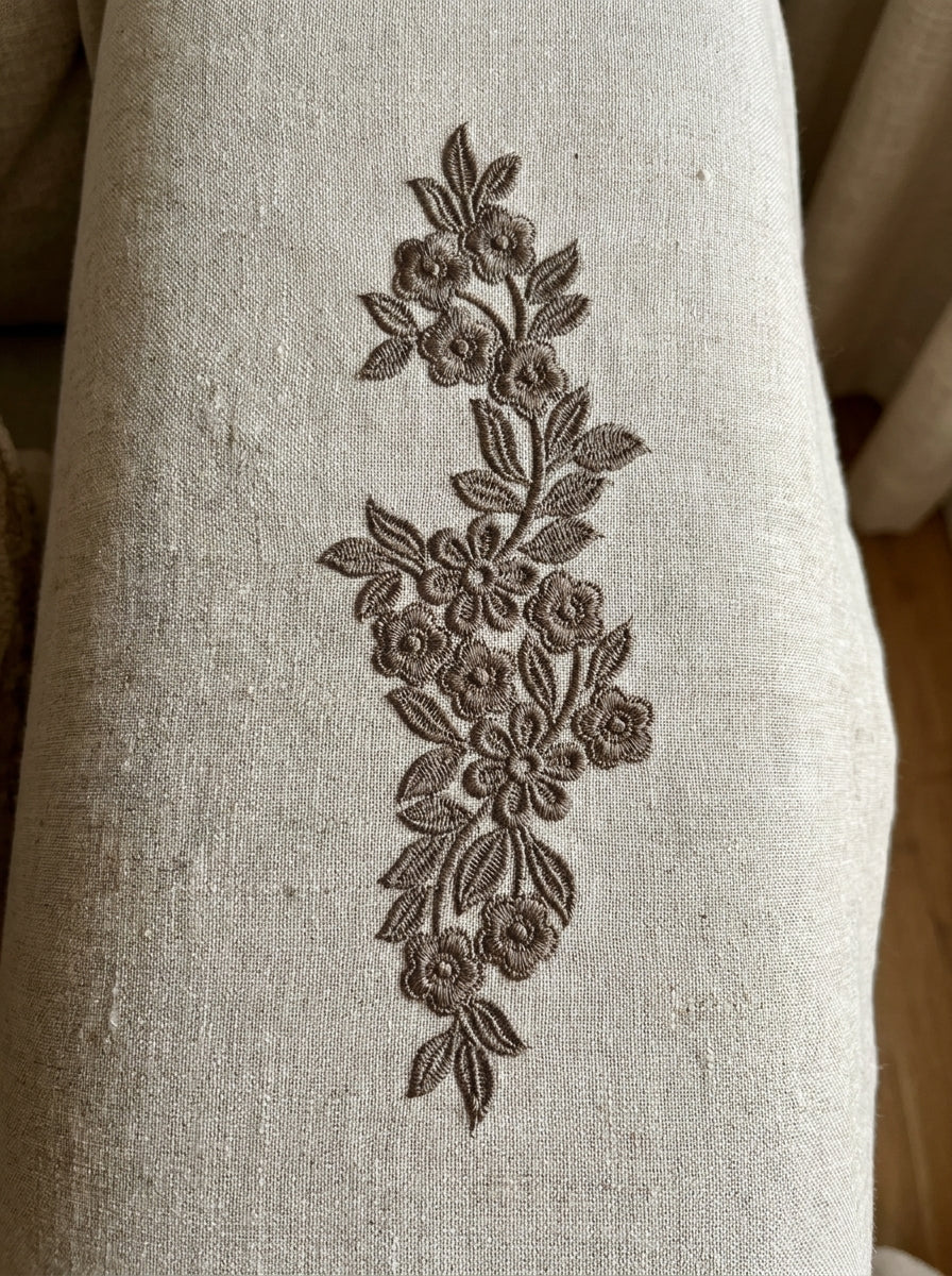 Close-up stitch detail of floral vine border machine embroidery on textured fabric.