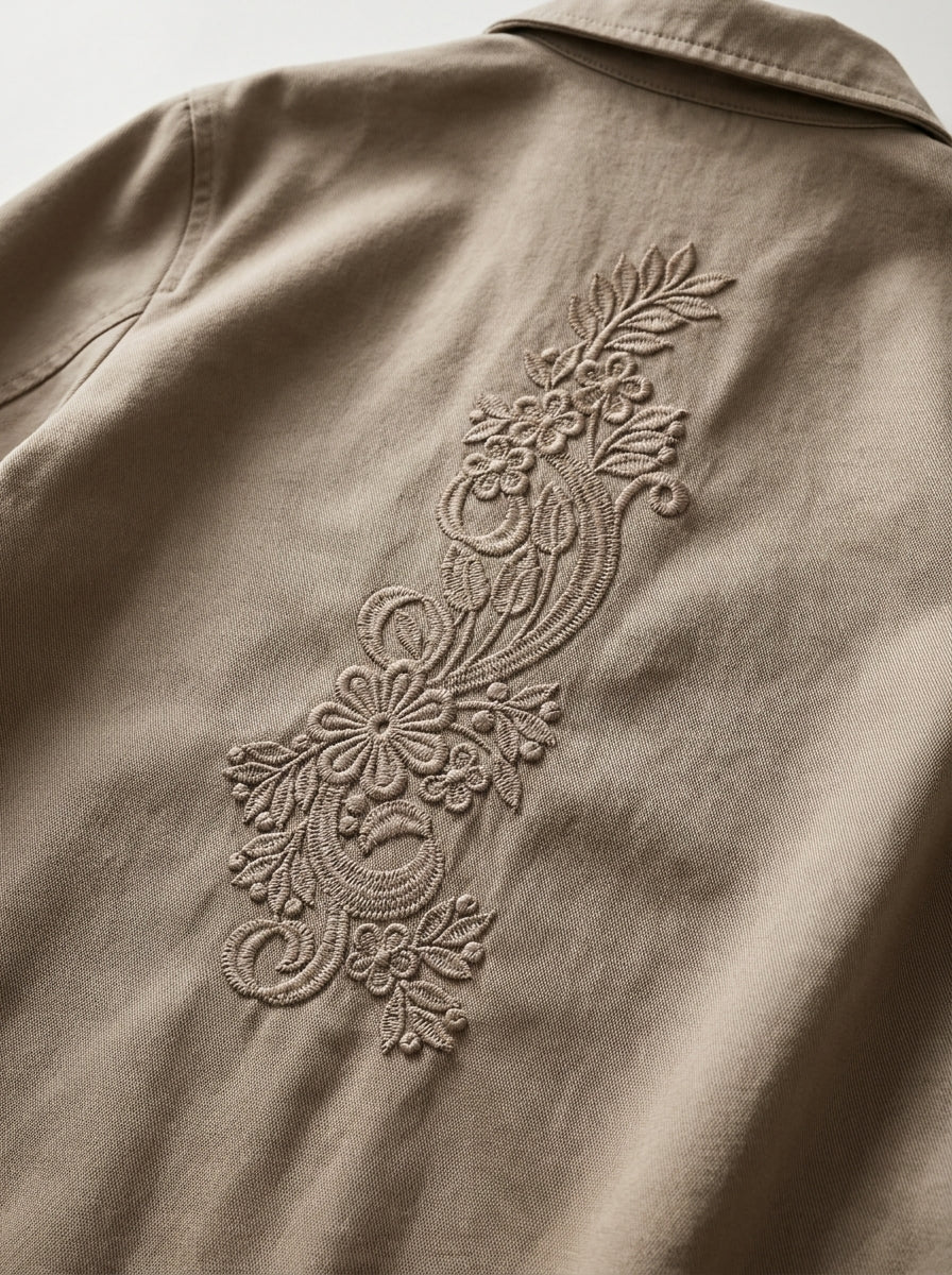 White decorative pillow with a light tan vertical floral border of embroidered flowers and leaves.