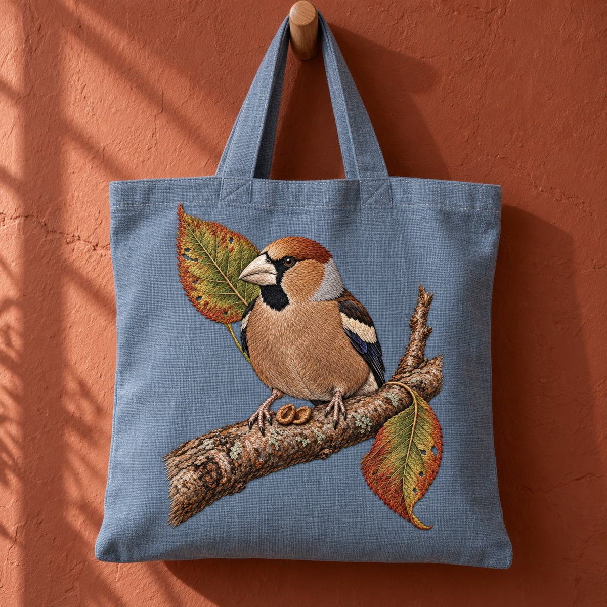 Hawfinch at the Cracked Cherry Stone visual mockup shown on the front of a structured linen tote, with the design on muted pale blue-grey linen.