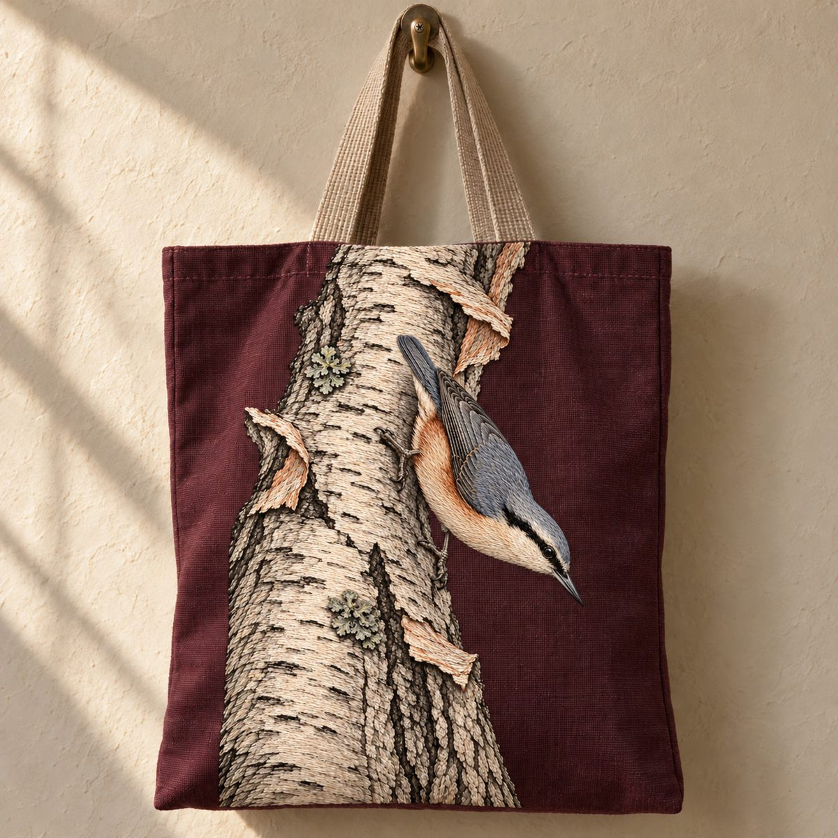 Nuthatch Descending the Silver Bark visual mockup shown on the front of a structured linen tote, with the design on muted burgundy linen.