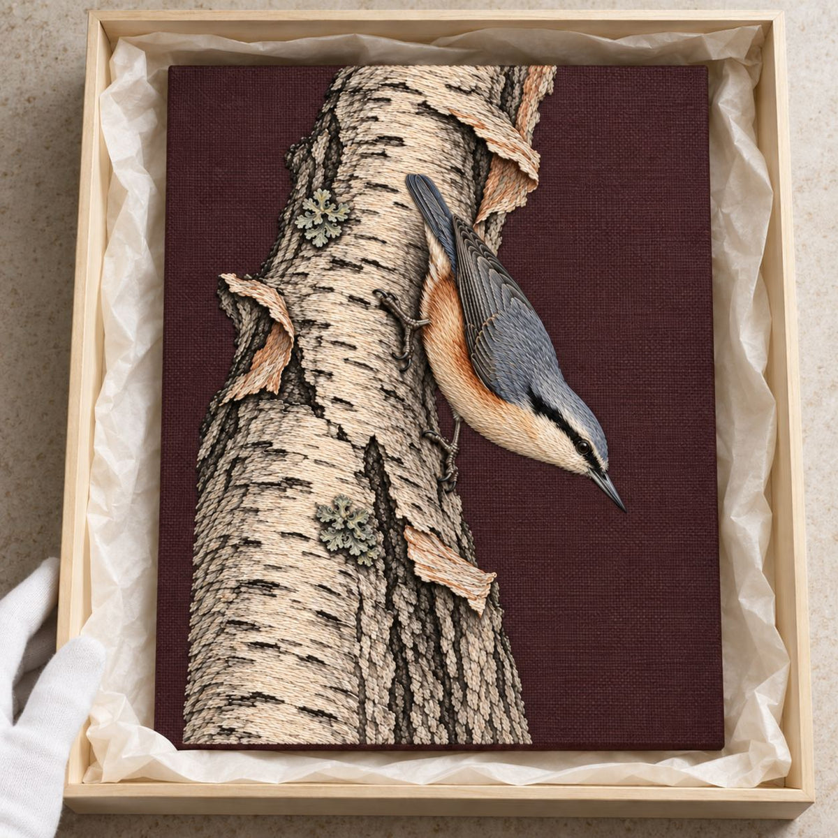 Nuthatch Descending the Silver Bark visual mockup shown as a textile panel in a collection tray, with the design on muted burgundy linen.