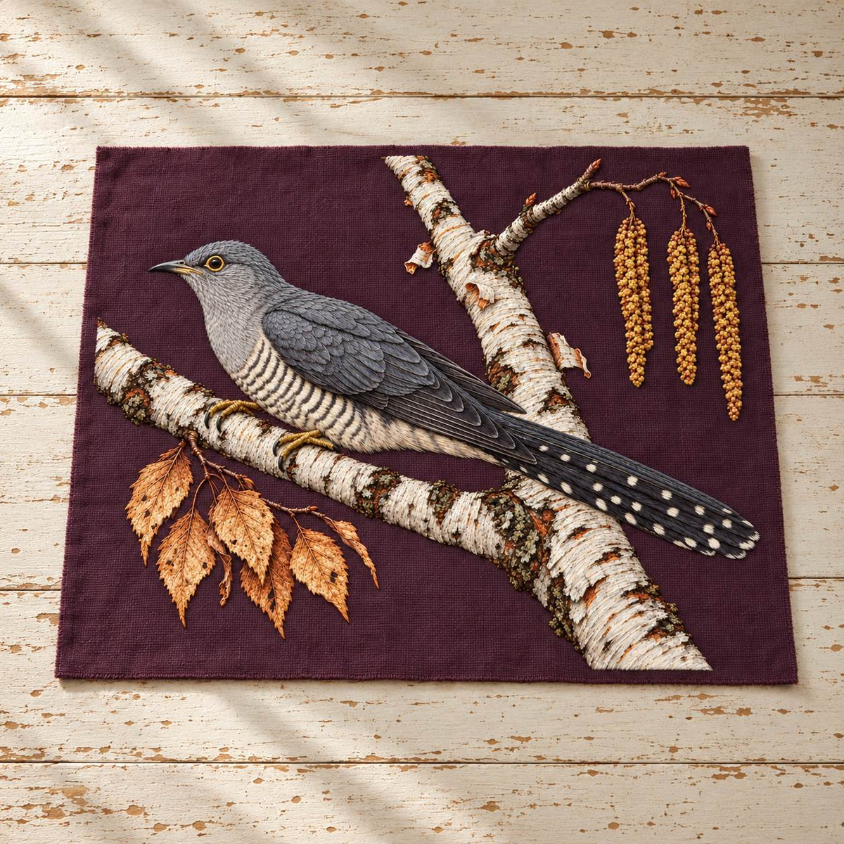Cuckoo Beyond the Birch Fork visual mockup shown as a textile panel on a stone platform, with the design on burgundy linen.