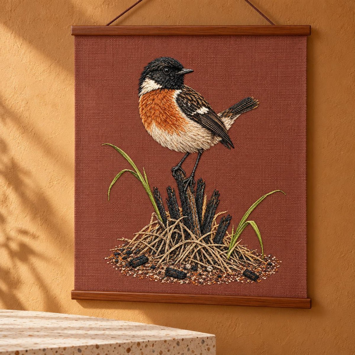 Stonechat at the Charred Grass Knot visual mockup shown as a hanging textile held by wooden rails, with the design on terracotta linen.