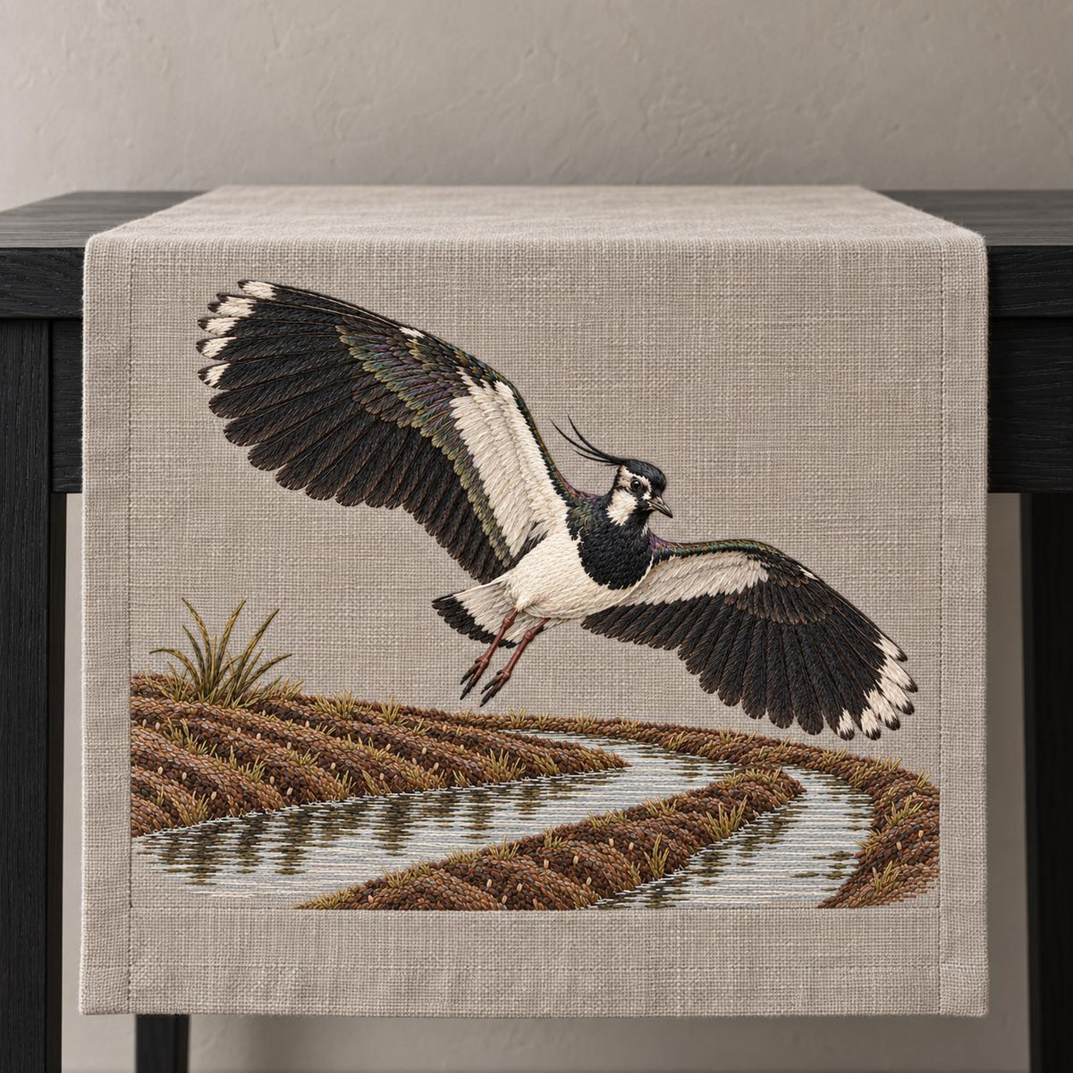 Lapwing Over the Wet Furrow visual mockup shown on a textile runner over a console, with the design on warm grey linen.