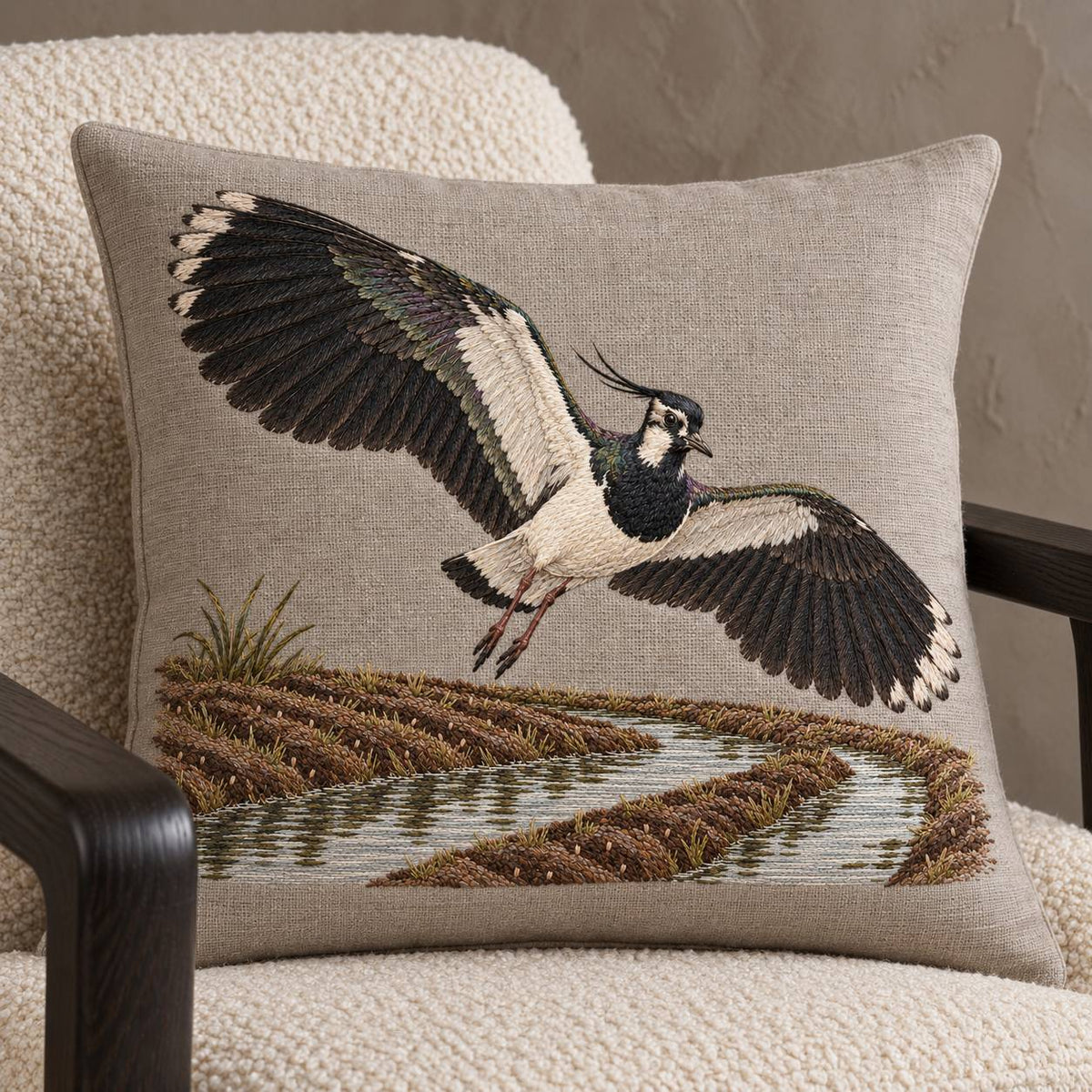 Lapwing Over the Wet Furrow visual mockup shown on a cushion in a lounge chair, with the design on warm grey linen.