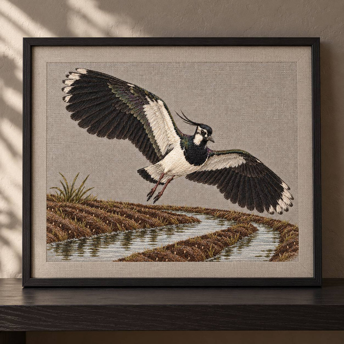 Lapwing Over the Wet Furrow visual mockup shown in a frame leaning on a mantel, with the design on warm grey linen.