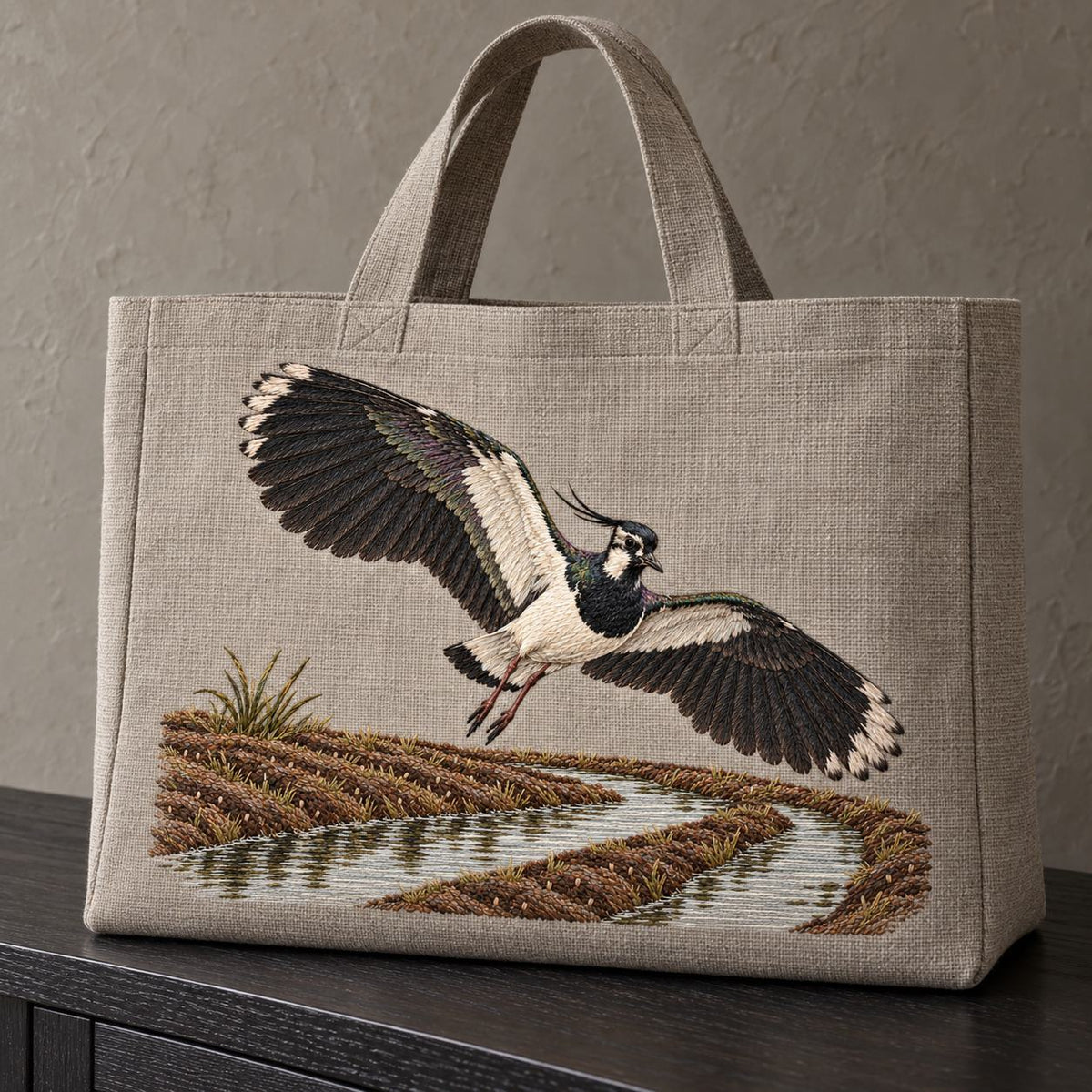 Lapwing Over the Wet Furrow visual mockup shown on the front of a structured linen tote, with the design on warm grey linen.