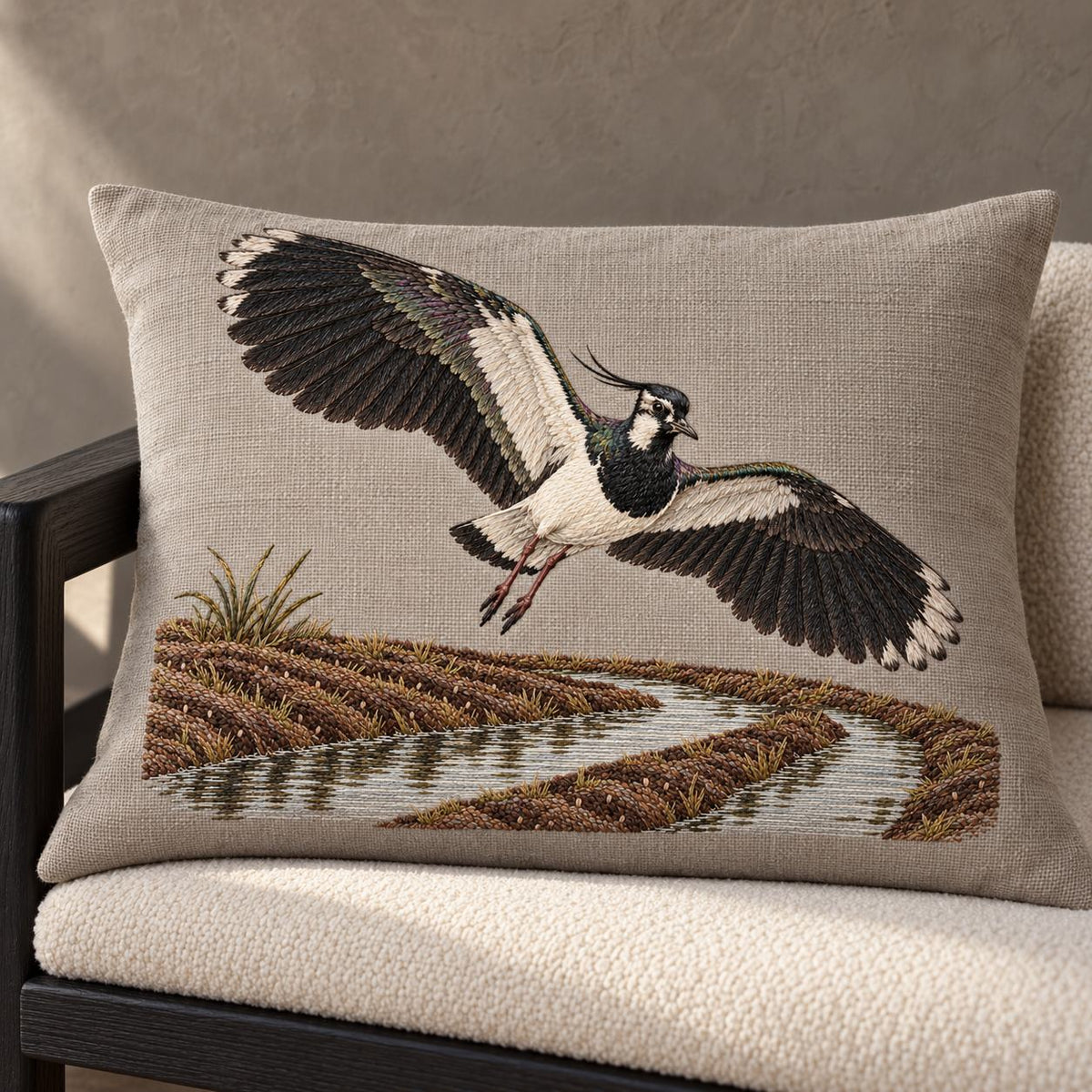 Lapwing Over the Wet Furrow visual mockup shown on a cushion beside a window, with the design on warm grey linen.