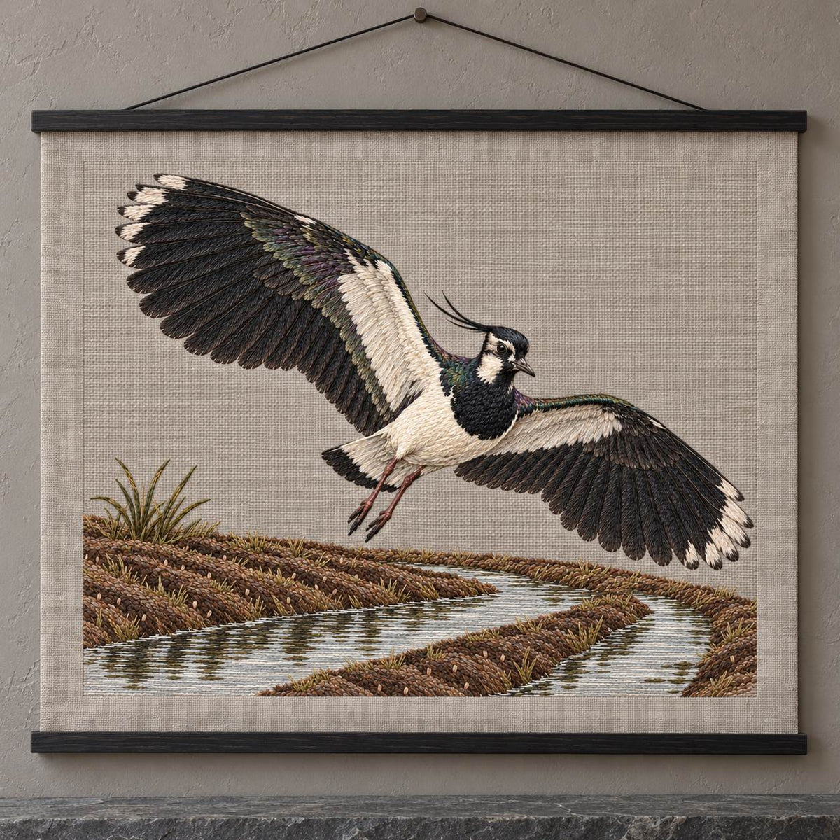 Lapwing Over the Wet Furrow visual mockup shown as a hanging textile held by wooden rails, with the design on warm grey linen.