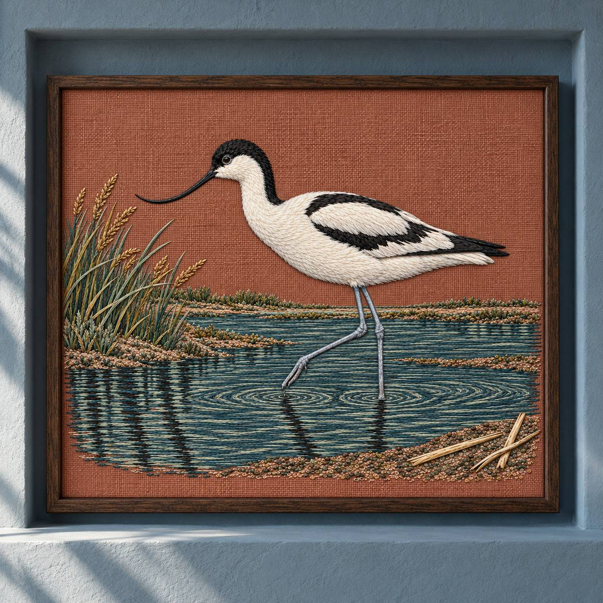 Avocet Across the Blackwater Line visual mockup shown as a framed textile in a gallery niche, with the design on dusty terracotta linen.