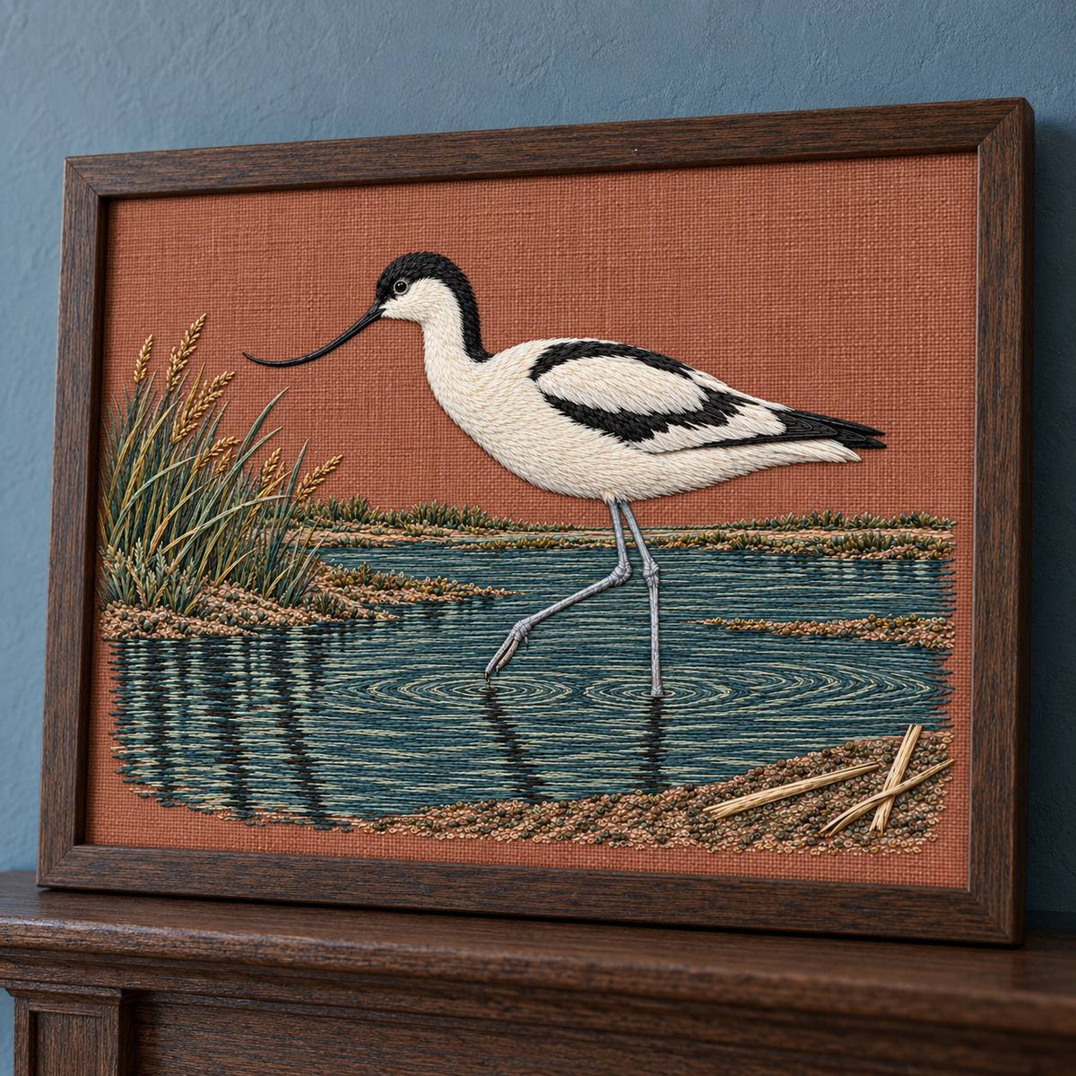 Avocet Across the Blackwater Line visual mockup shown in a frame leaning on a mantel, with the design on dusty terracotta linen.
