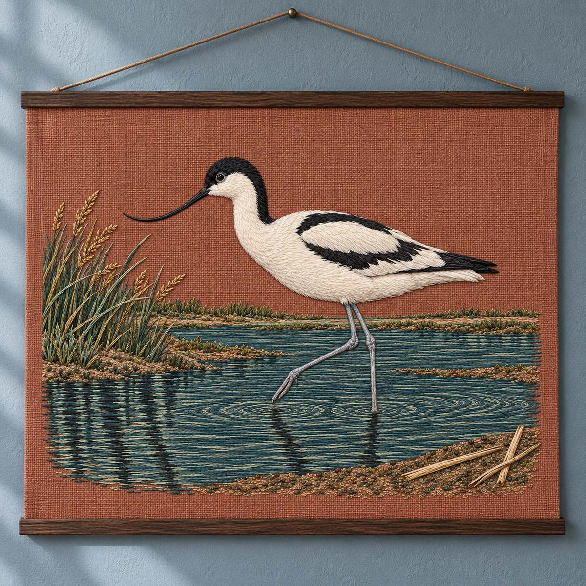 Avocet Across the Blackwater Line visual mockup shown as a hanging textile held by wooden rails, with the design on dusty terracotta linen.