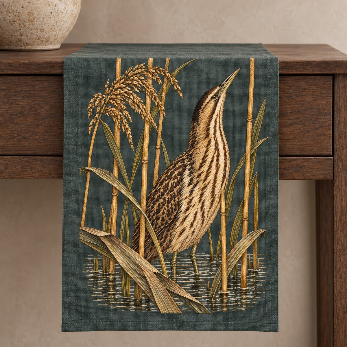 Bittern Behind the Ochre Reed Veil visual mockup shown on a textile runner over a console, with the design on dark muted green linen.