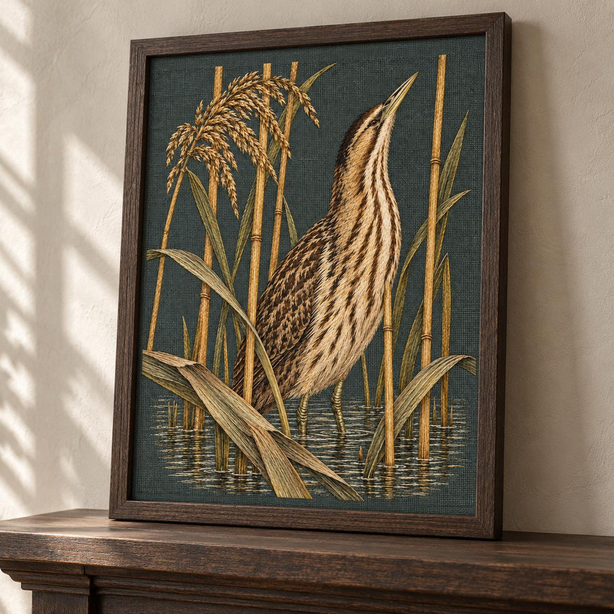 Bittern Behind the Ochre Reed Veil visual mockup shown in a frame leaning on a mantel, with the design on dark muted green linen.