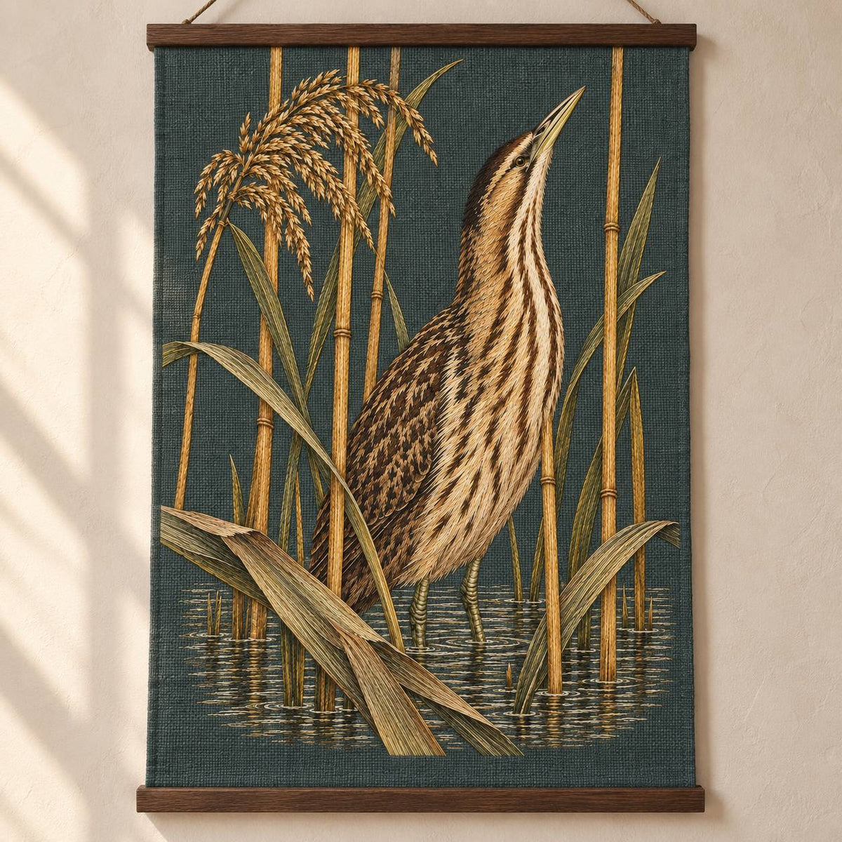 Bittern Behind the Ochre Reed Veil visual mockup shown as a hanging textile held by wooden rails, with the design on dark muted green linen.