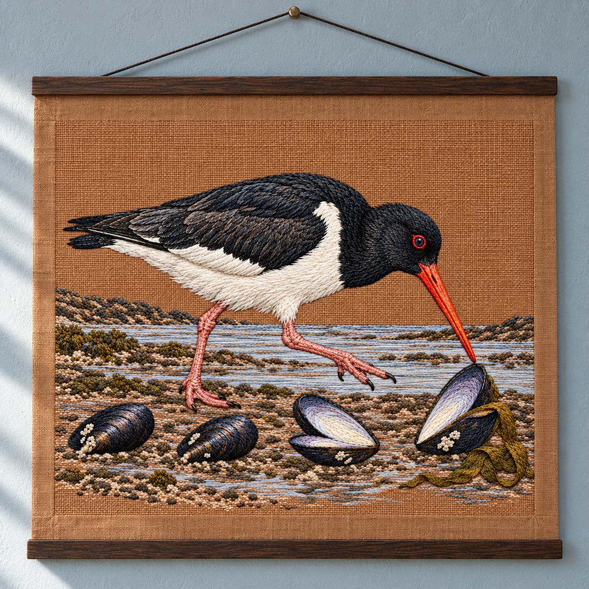 Oystercatcher Across the Mussel Line visual mockup shown as a hanging textile held by wooden rails, with the design on warm ochre linen.