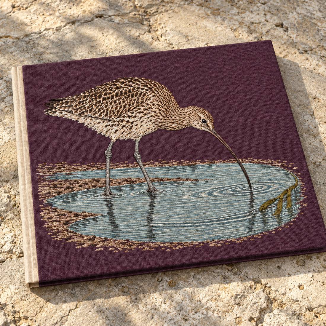 Curlew Under the Long Tide Moon visual mockup shown on a cloth portfolio cover, with the design on deep plum linen.