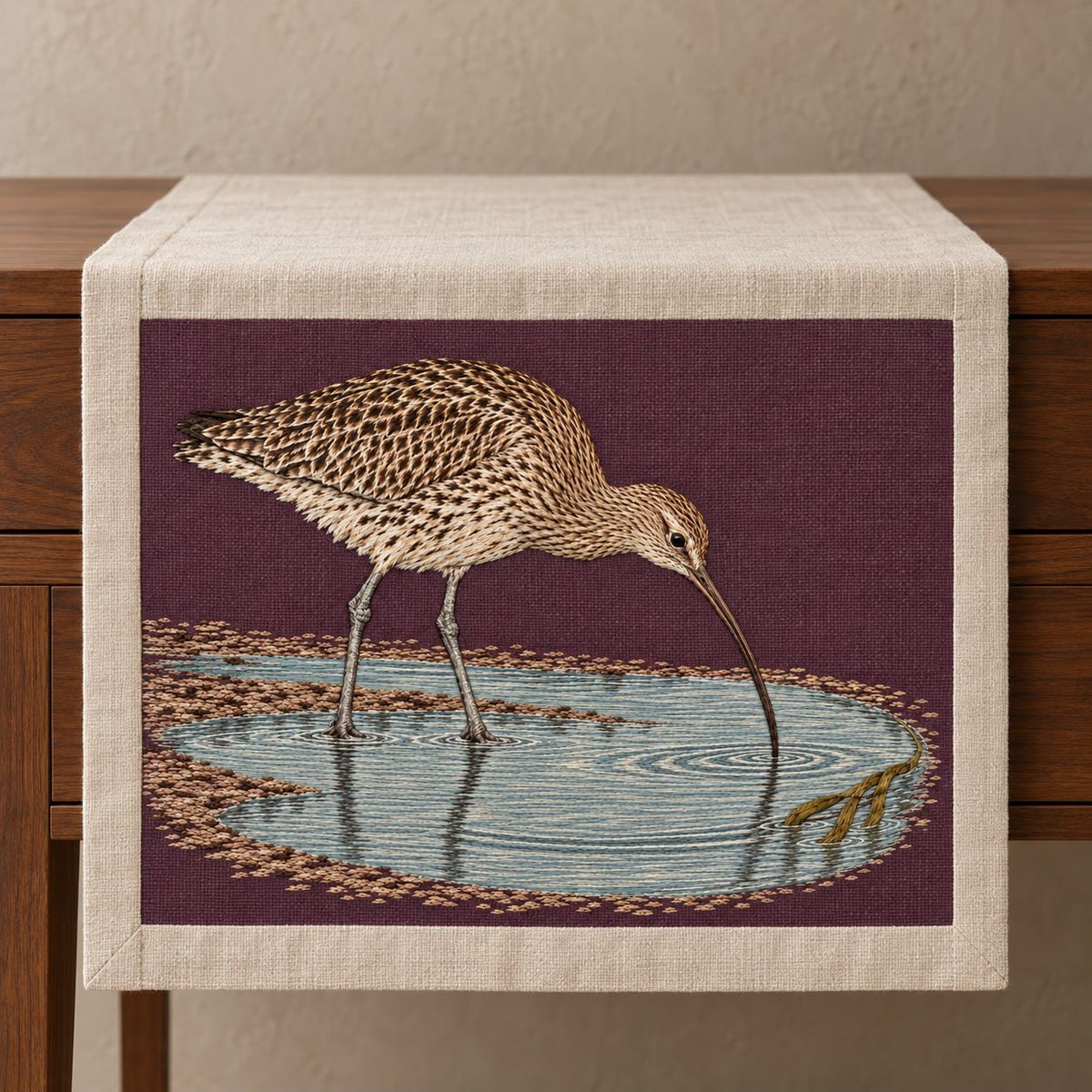 Curlew Under the Long Tide Moon visual mockup shown on a textile runner over a console, with the design on deep plum linen.