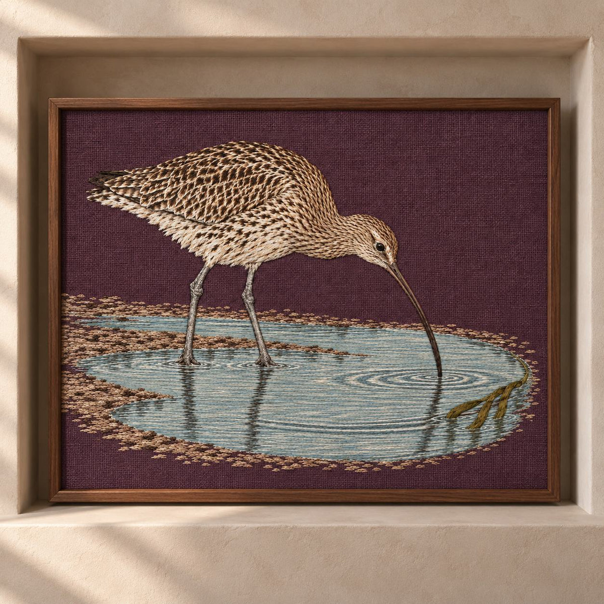 Curlew Under the Long Tide Moon visual mockup shown as a framed textile in a gallery niche, with the design on deep plum linen.