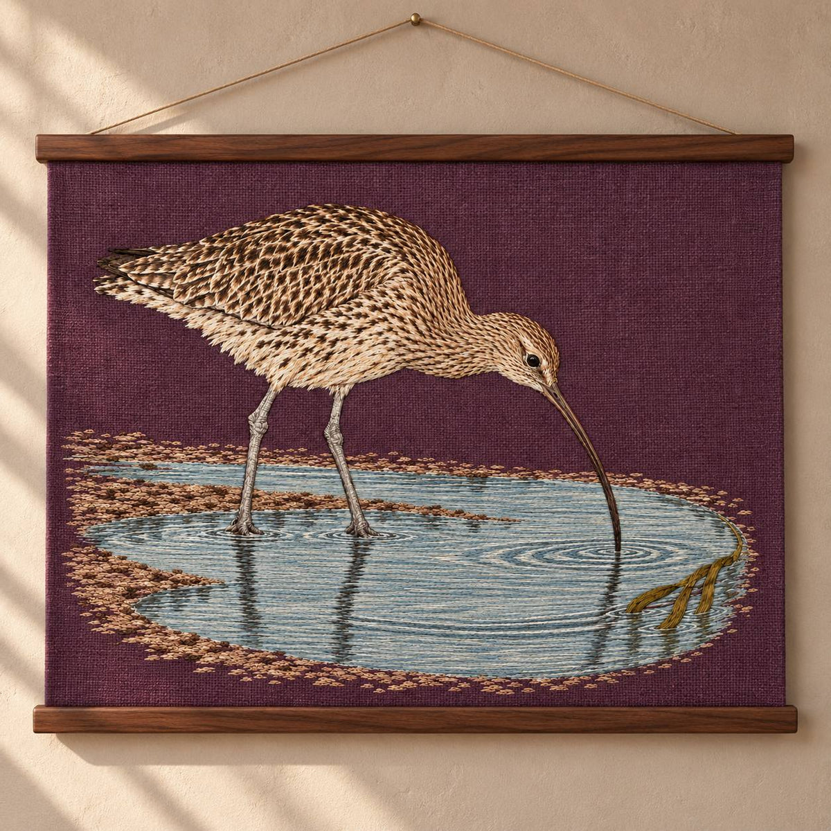 Curlew Under the Long Tide Moon visual mockup shown as a hanging textile held by wooden rails, with the design on deep plum linen.