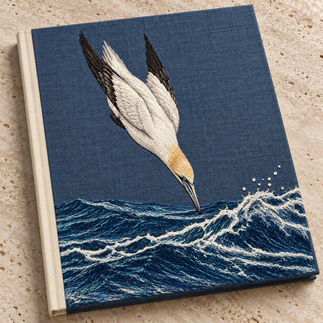Gannet in the Whitewater Plunge visual mockup shown on a cloth portfolio cover, with the design on slate-blue linen.