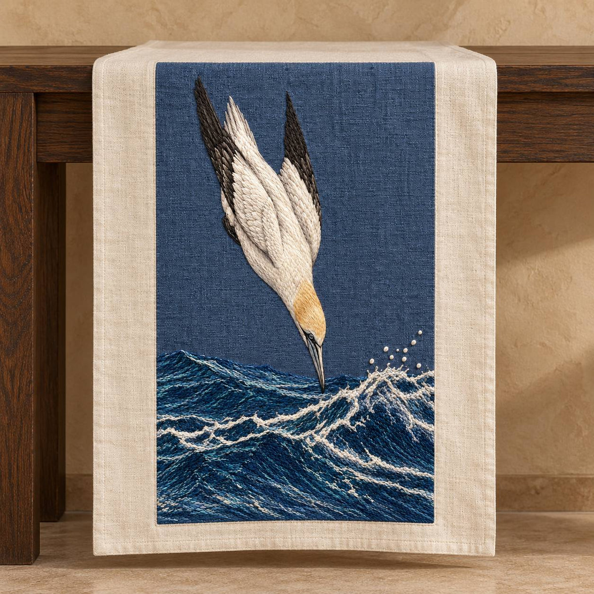 Gannet in the Whitewater Plunge visual mockup shown on a textile runner over a console, with the design on slate-blue linen.
