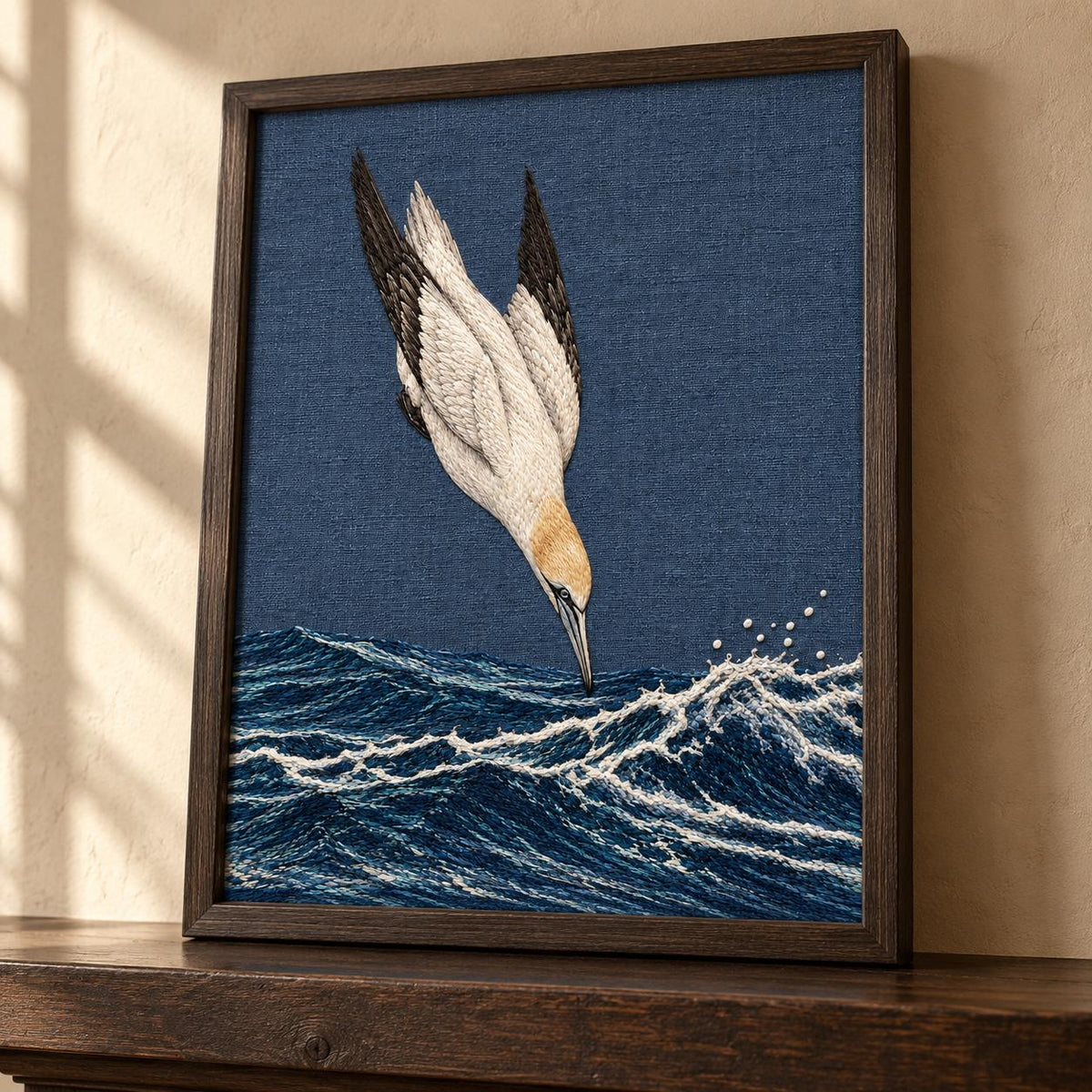 Gannet in the Whitewater Plunge visual mockup shown in a frame leaning on a mantel, with the design on slate-blue linen.