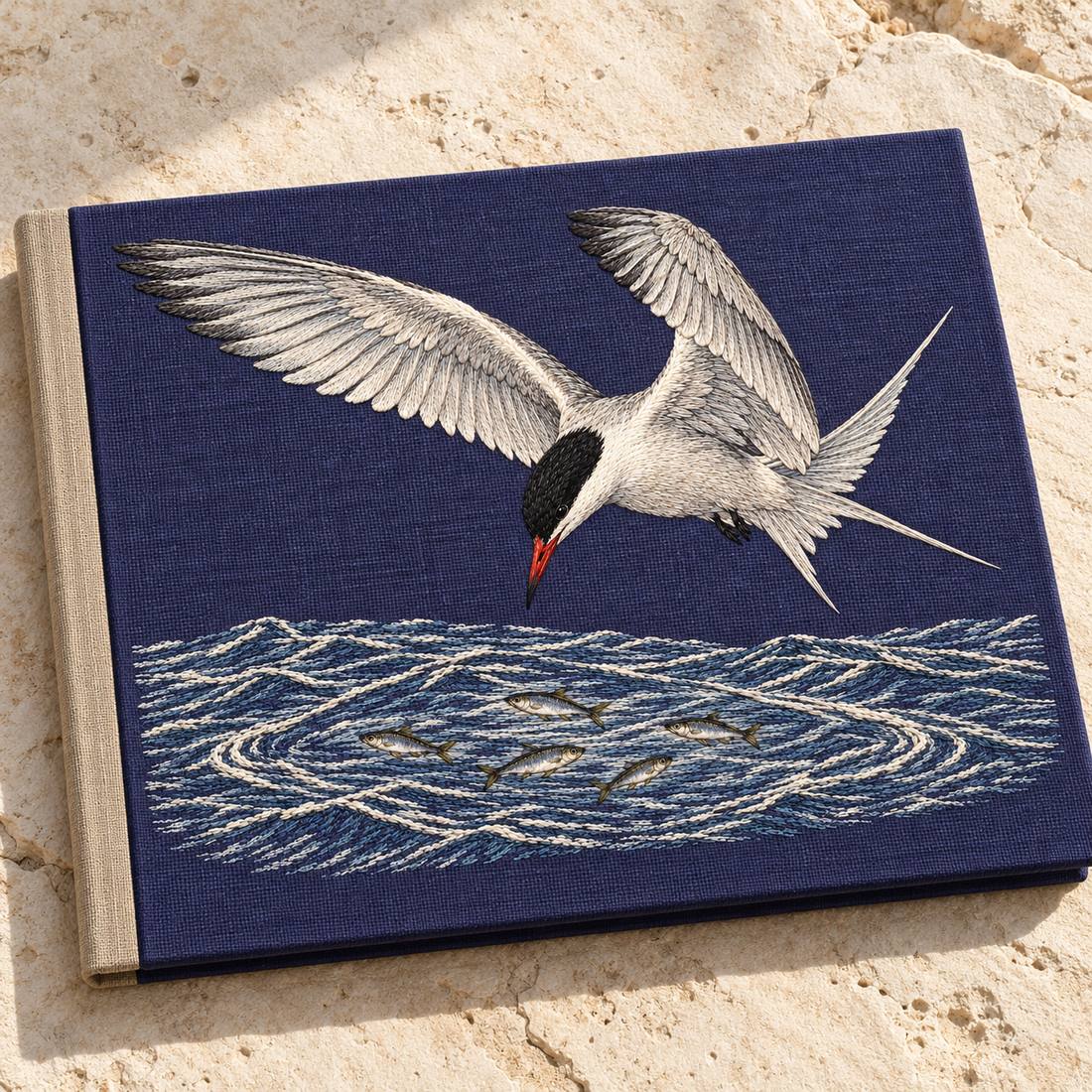 Common Tern Above the Silver Shoal visual mockup shown on a cloth portfolio cover, with the design on deep blue-violet linen.