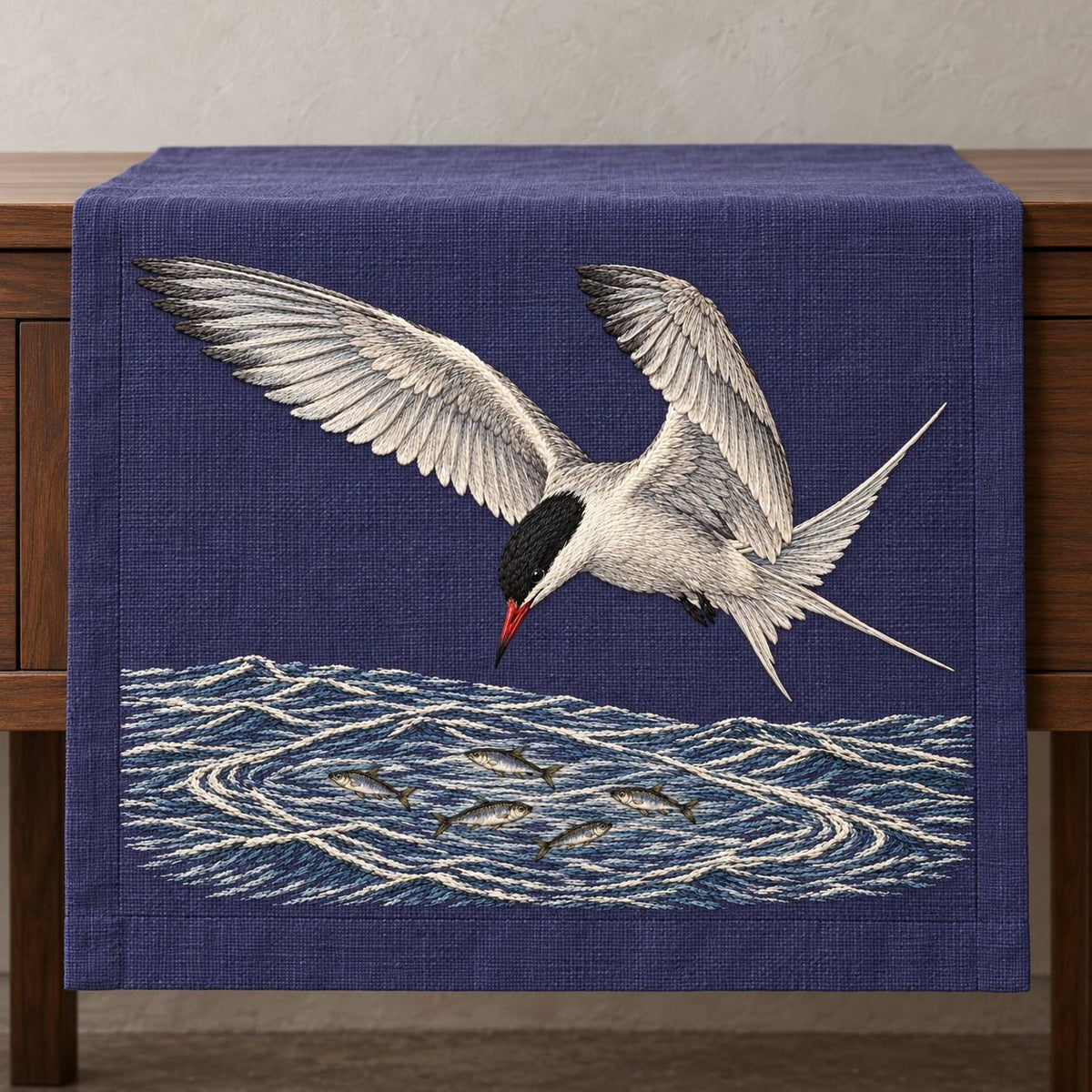Common Tern Above the Silver Shoal visual mockup shown on a textile runner over a console, with the design on deep blue-violet linen.