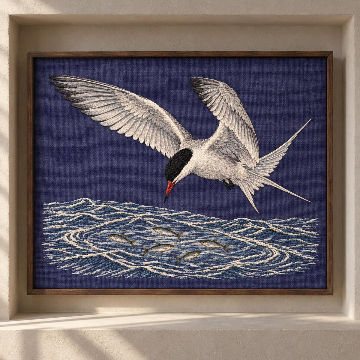 Common Tern Above the Silver Shoal visual mockup shown as a framed textile in a gallery niche, with the design on deep blue-violet linen.