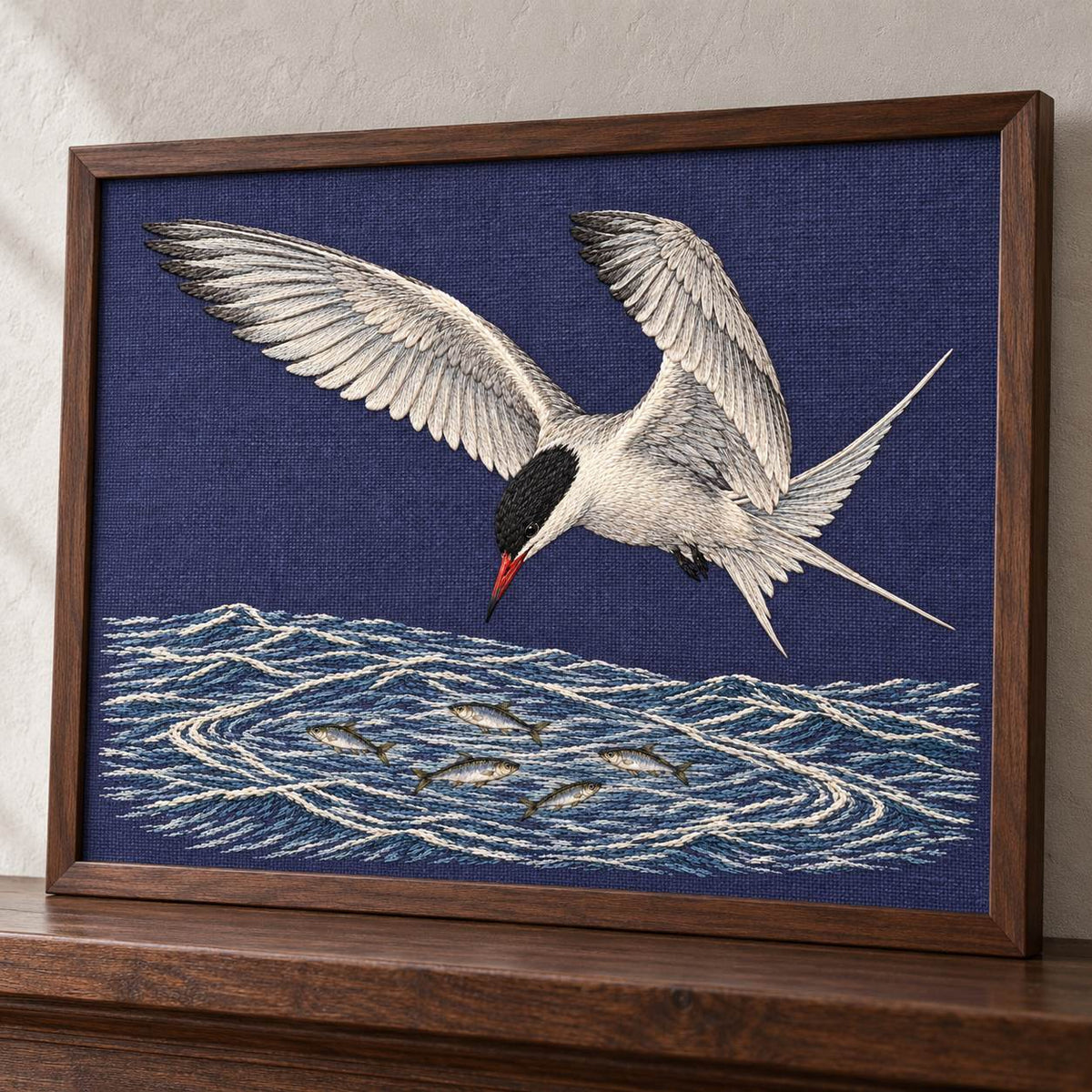 Common Tern Above the Silver Shoal visual mockup shown in a frame leaning on a mantel, with the design on deep blue-violet linen.