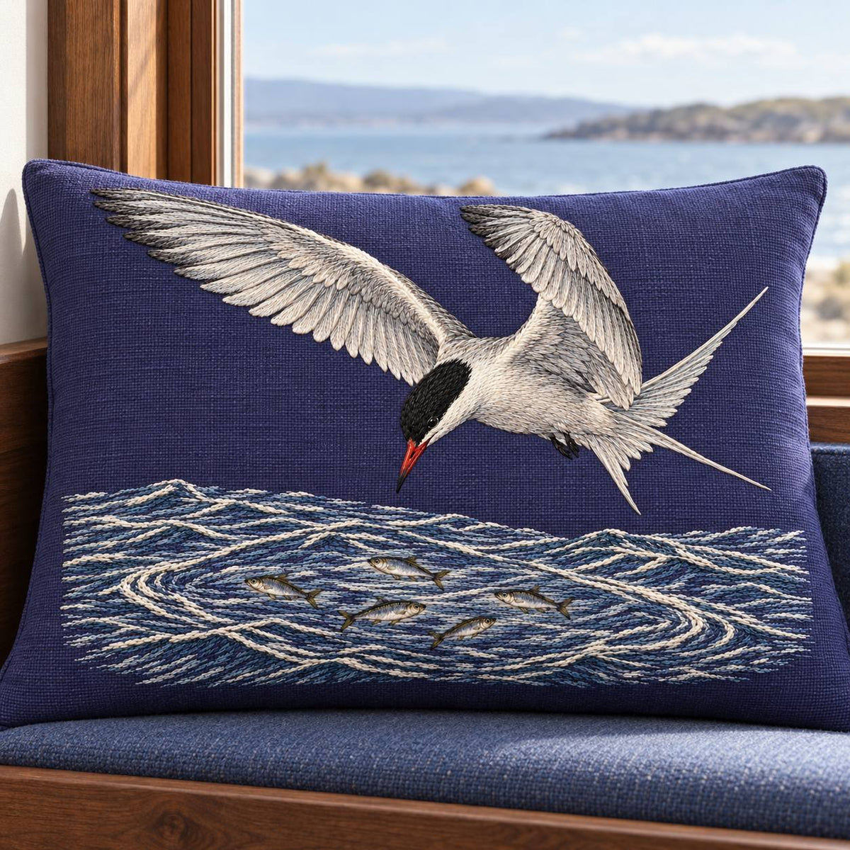 Common Tern Above the Silver Shoal visual mockup shown on a cushion beside a window, with the design on deep blue-violet linen.