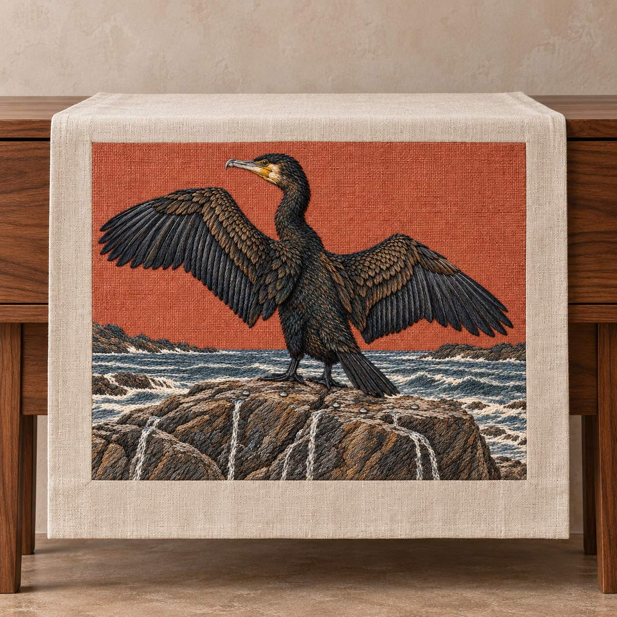 Cormorant Opening the Rain Black Wings visual mockup shown on a textile runner over a console, with the design on muted rust linen.