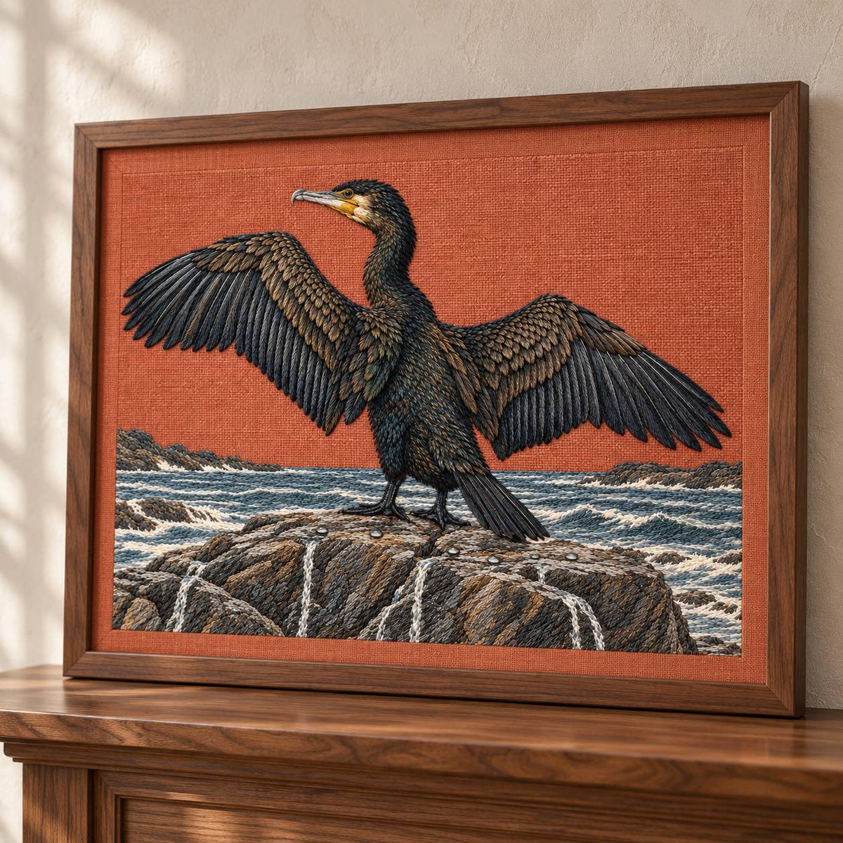 Cormorant Opening the Rain Black Wings visual mockup shown in a frame leaning on a mantel, with the design on muted rust linen.