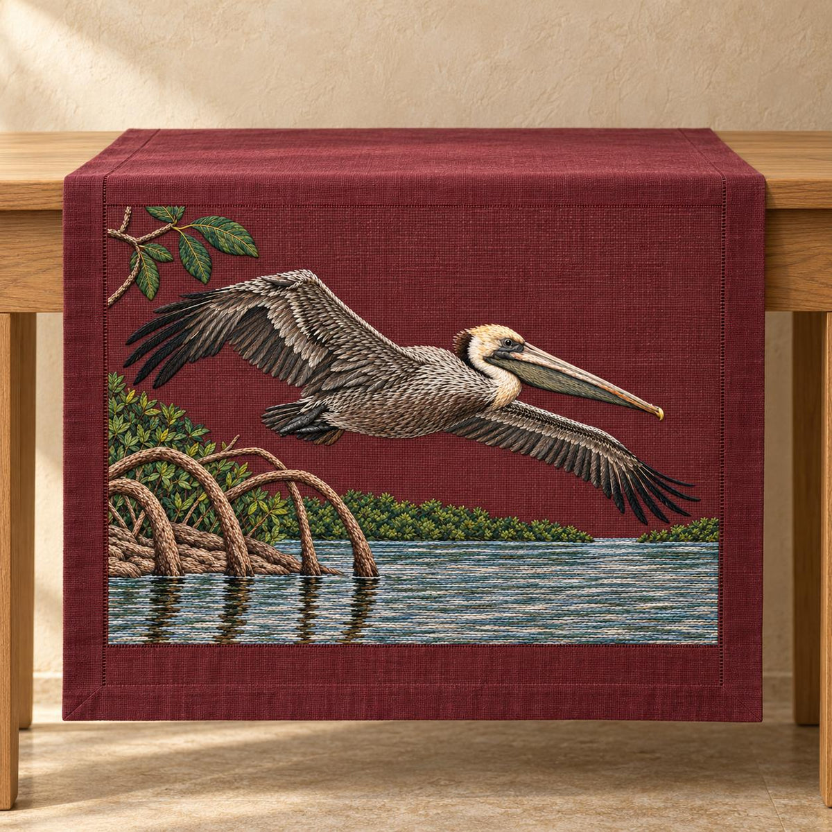 Pelican Over the Mangrove Mirror visual mockup shown on a textile runner over a console, with the design on deep burgundy linen.