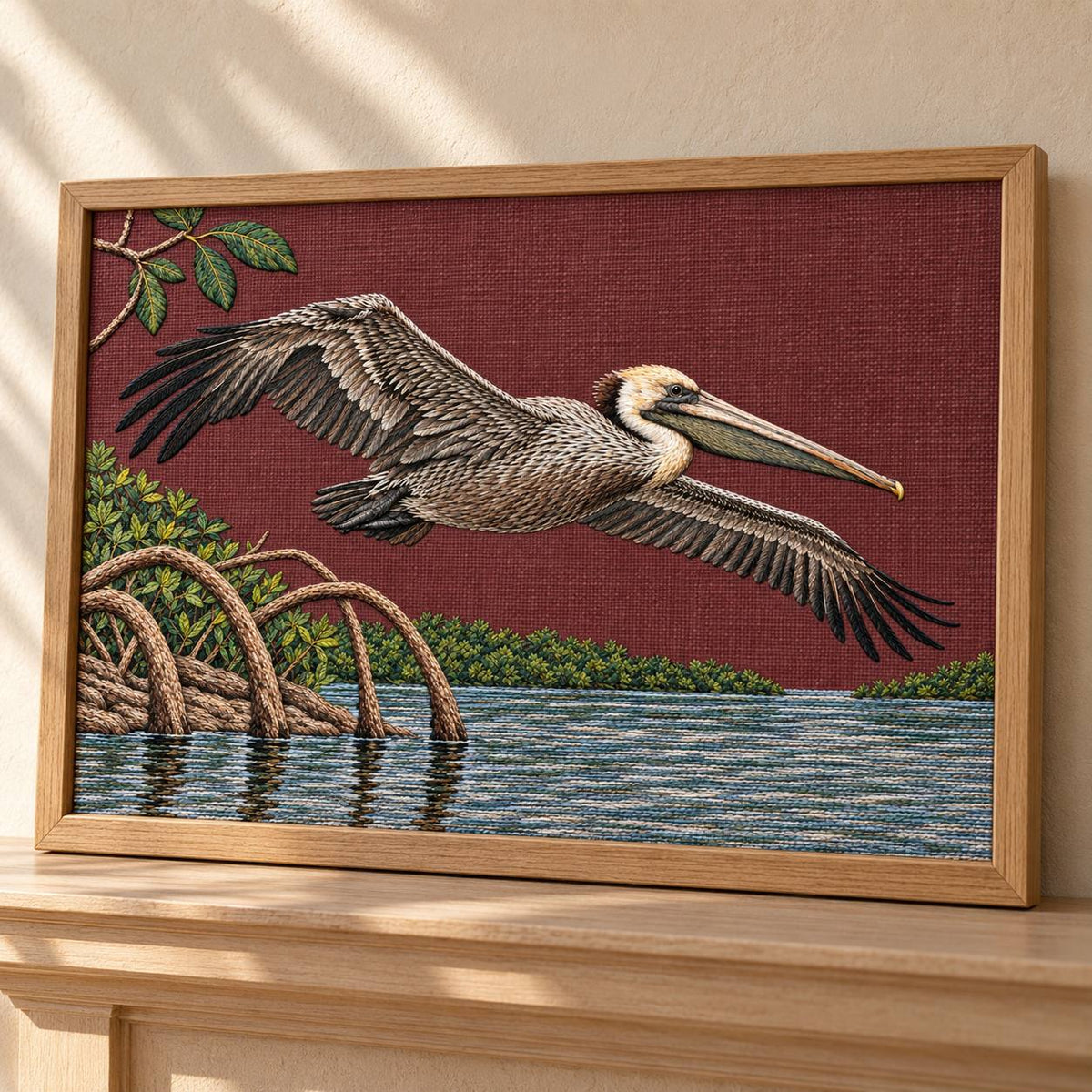 Pelican Over the Mangrove Mirror visual mockup shown in a frame leaning on a mantel, with the design on deep burgundy linen.