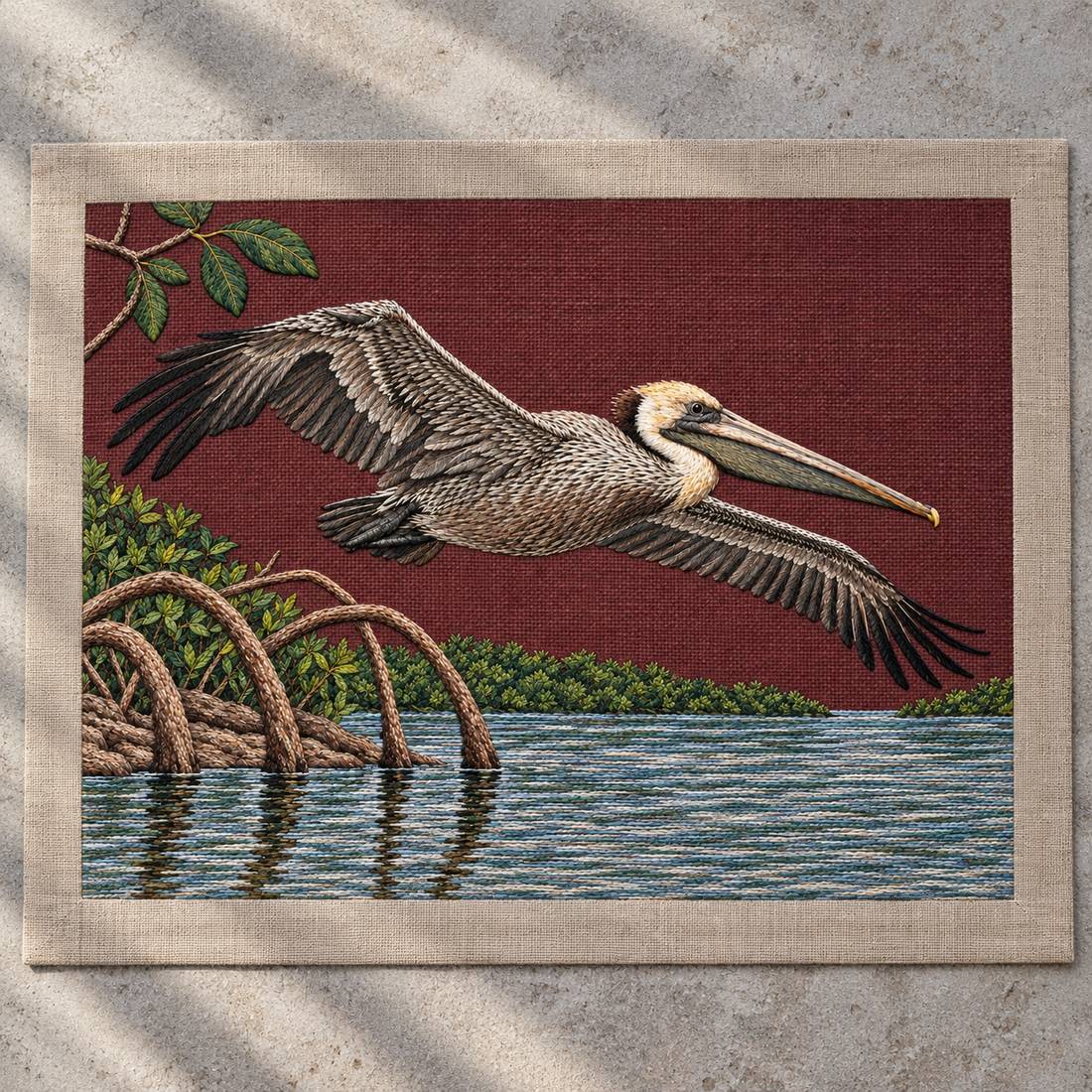 Pelican Over the Mangrove Mirror visual mockup shown as a textile panel on a stone platform, with the design on deep burgundy linen.