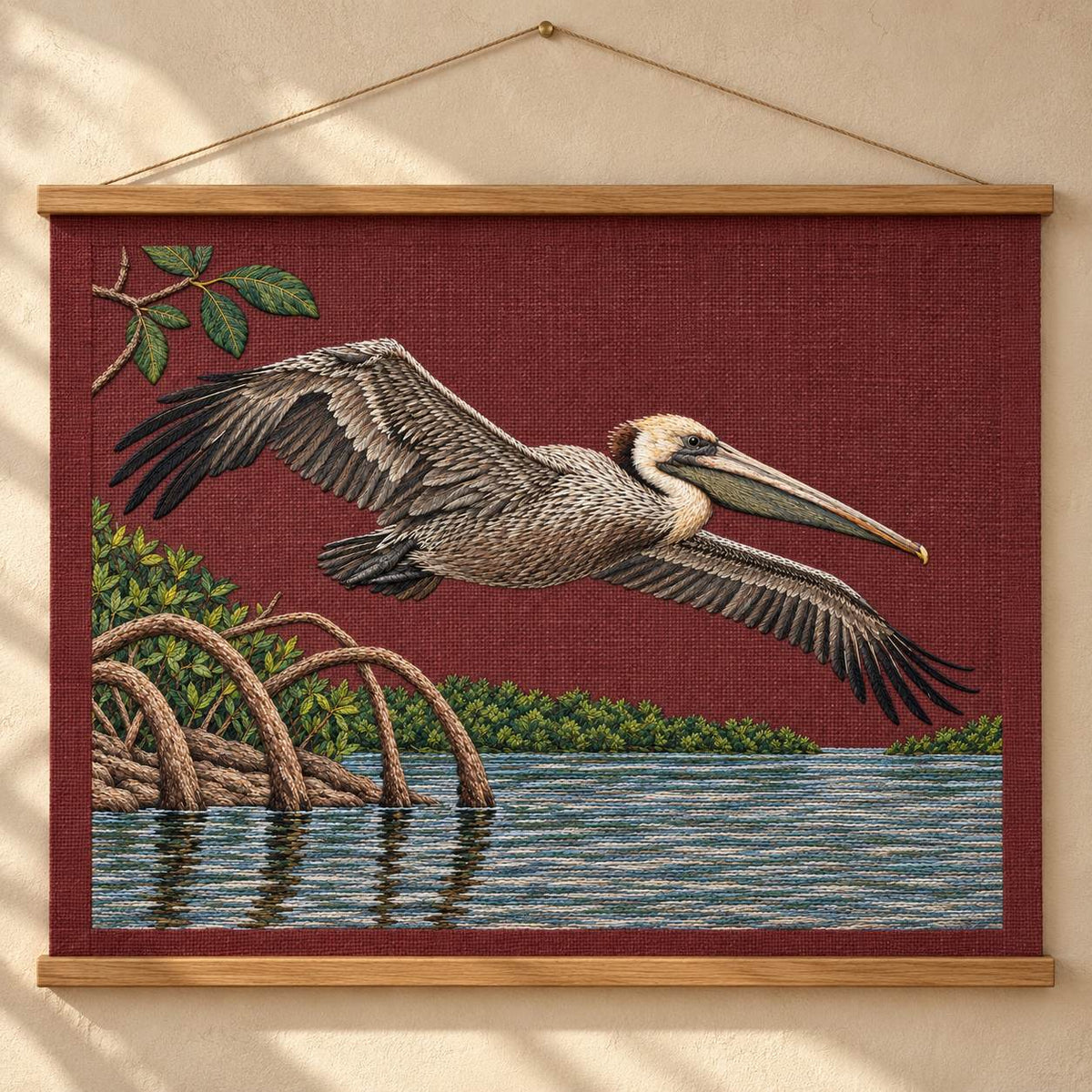 Pelican Over the Mangrove Mirror visual mockup shown as a hanging textile held by wooden rails, with the design on deep burgundy linen.