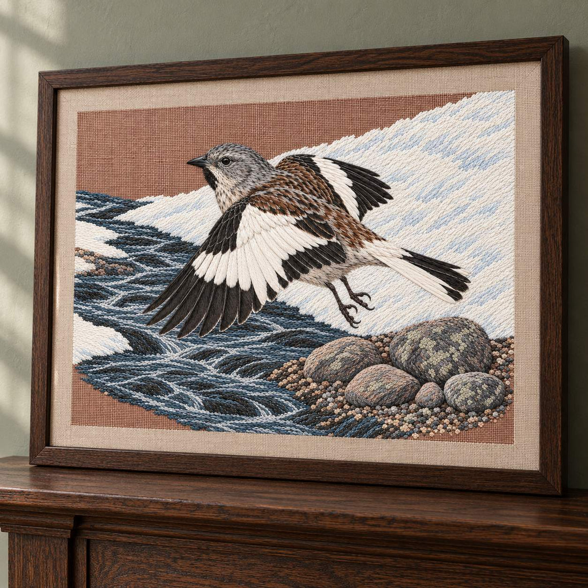 Snowfinch Along the Meltwater Cut visual mockup shown in a frame leaning on a mantel, with the design on warm oatmeal linen.