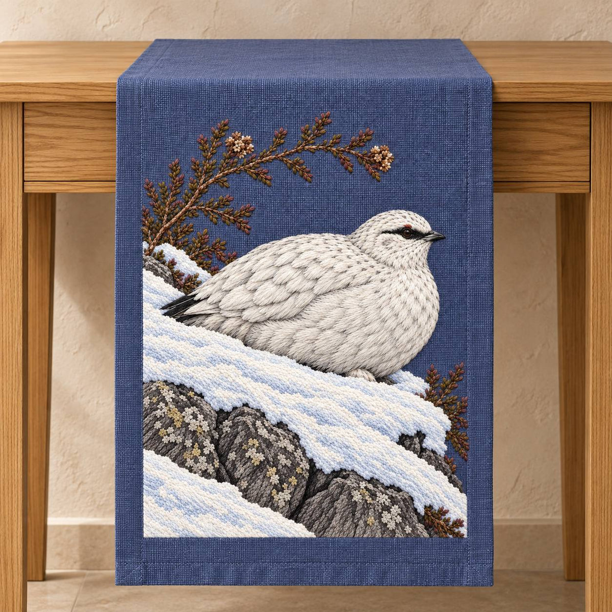 Ptarmigan Beneath the Wind Carved Heather visual mockup shown on a textile runner over a console, with the design on blue-violet linen.