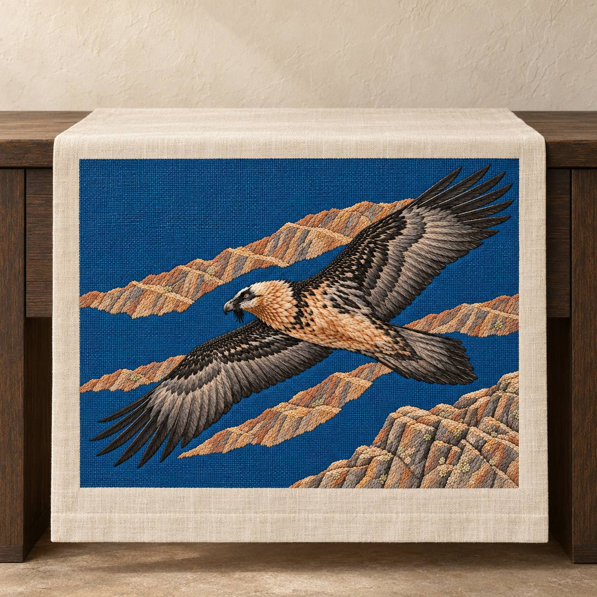Lammergeier Through the Ochre Updraft visual mockup shown on a textile runner over a console, with the design on deep blue linen.