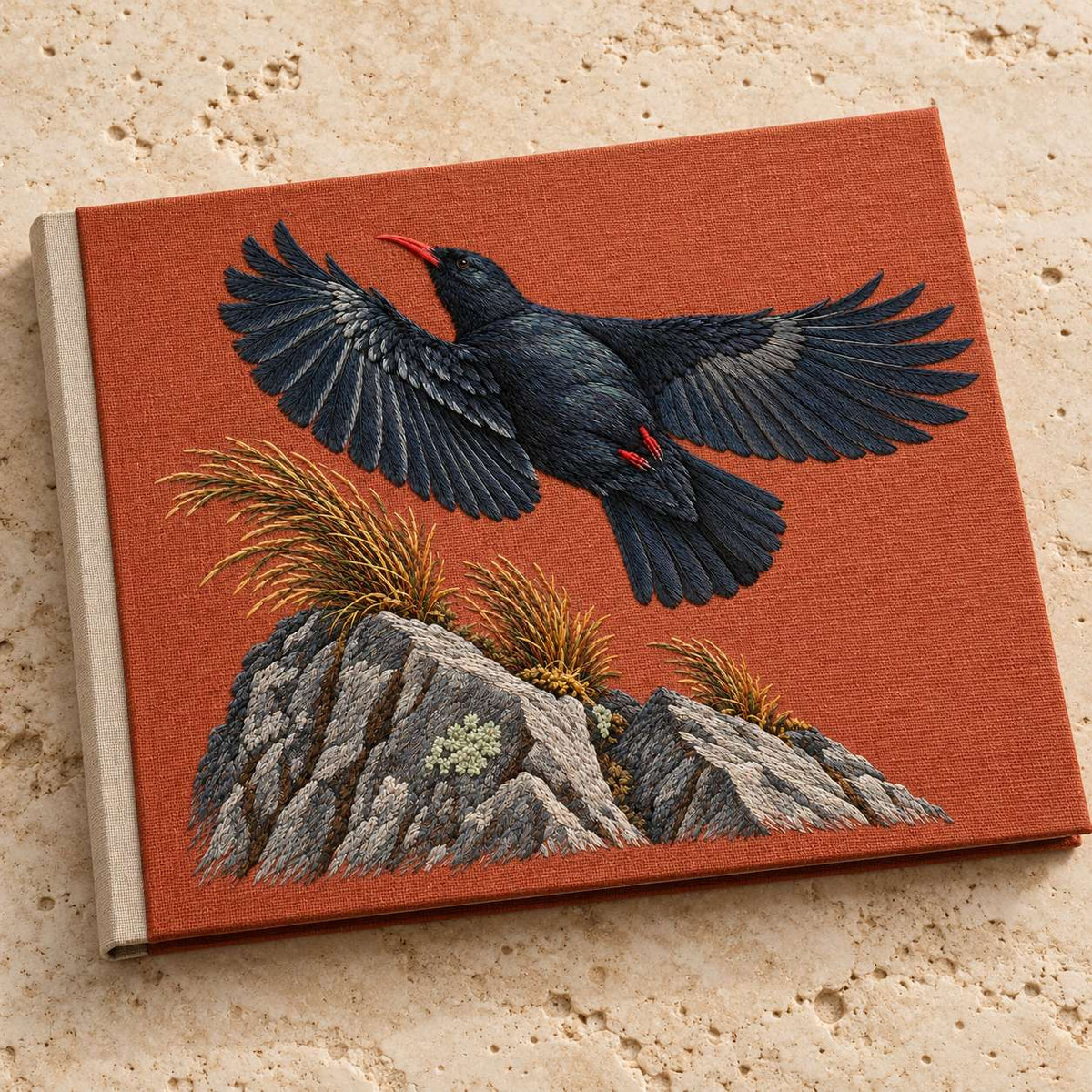 Chough at the Red Summit Flag visual mockup shown on a cloth portfolio cover, with the design on muted rust linen.