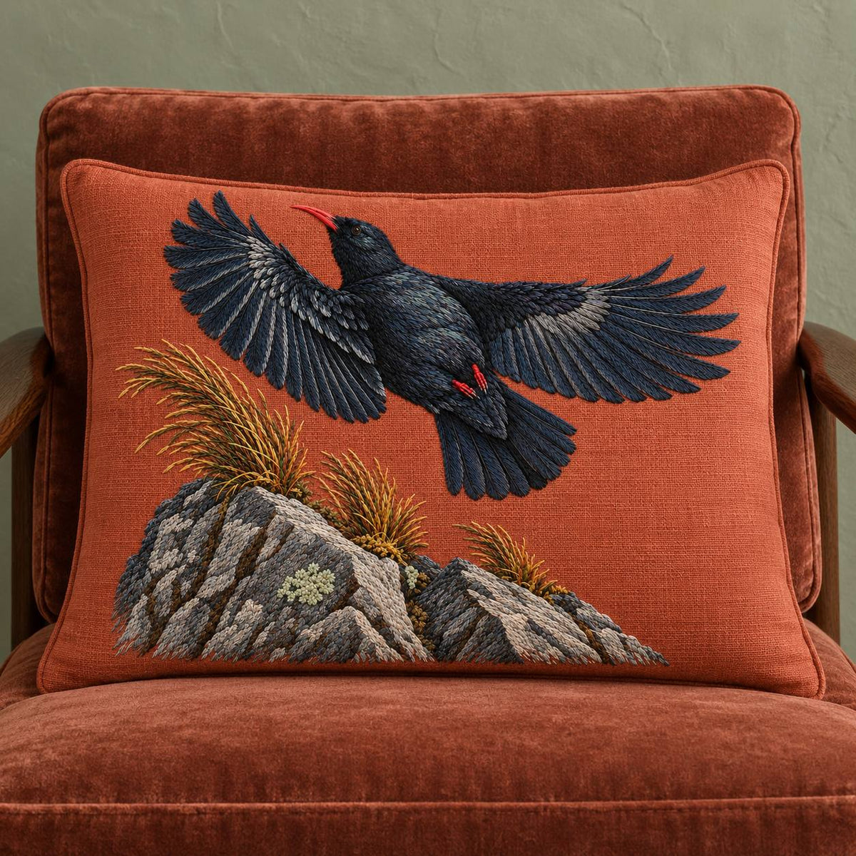 Chough at the Red Summit Flag visual mockup shown on a cushion in a lounge chair, with the design on muted rust linen.